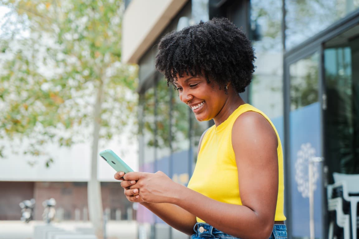 Woman smiling with her phone outside a modern building