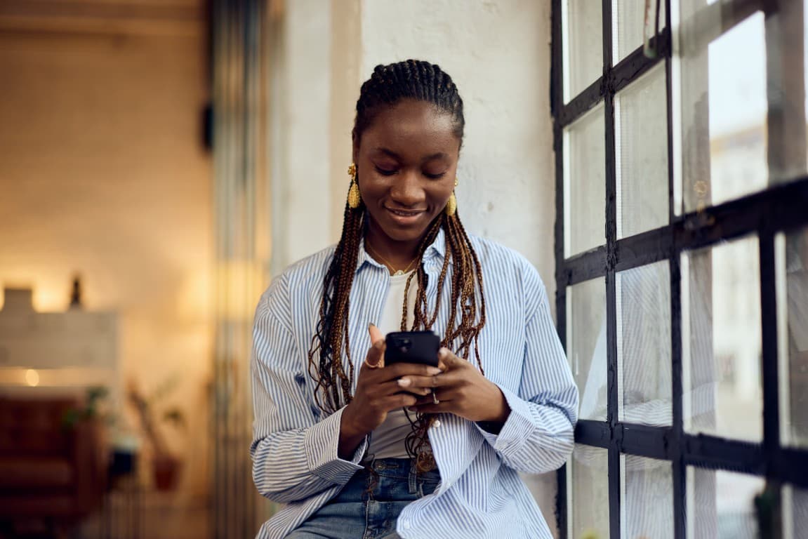 Young woman relaxing indoors by a window with her phone